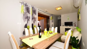 A dining area with a wooden table, white chairs, and a yellow tablecloth. There is a bottle of wine and a glass on the table. - Villa Belmondo- Three Bedroom Villa with Terrace and Private Pool (Gruda)