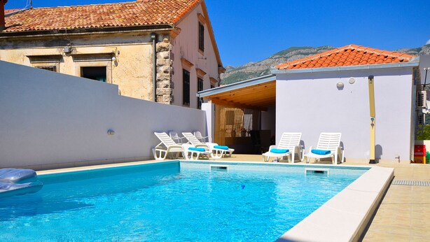 A swimming pool with lounge chairs, a white building with a red-tiled roof, and a mountainous backdrop. - Villa Belmondo- Three Bedroom Villa with Terrace and Private Pool (Gruda)