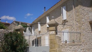 Un edificio de piedra con una entrada porticada, un muro de piedra y una pequeña maceta a la derecha.