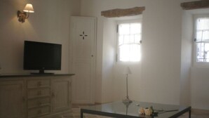 Sala de estar con televisor, mesa de centro de vidrio, aparador y puerta con diseño de cruz.