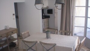 Comedor con una mesa dispuesta para cuatro personas, rodeada de sillas, una mesita auxiliar y una planta en maceta.