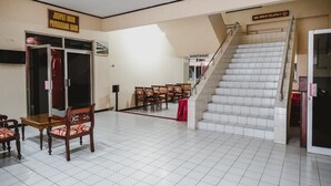 A spacious room with a staircase leading to an upper level, a reception desk, and a sign indicating a secretariat area. - RedDoorz @ Ungaran (Ungaran)
