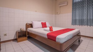 A hotel room with a wooden bed, white tiled walls, a small wooden nightstand, and a window with blue curtains. - RedDoorz @ Ungaran (Ungaran)