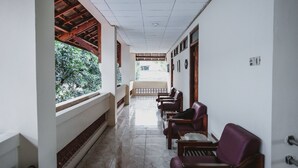 A corridor with a tiled floor, wooden chairs, a bench, and a view of greenery outside. - RedDoorz @ Ungaran (Ungaran)