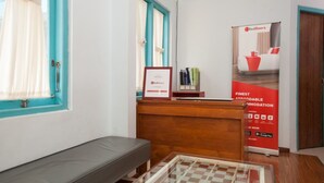 Et hotelreceptionsområde med en trædisk, et indrammet certifikat og en RedDoorz-annoncering.