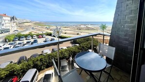 A balcony with a view of the sea, a parking area, and a building with a stone facade. - Cozy studio near the beach with balcony (Les Sables-d'Olonne)
