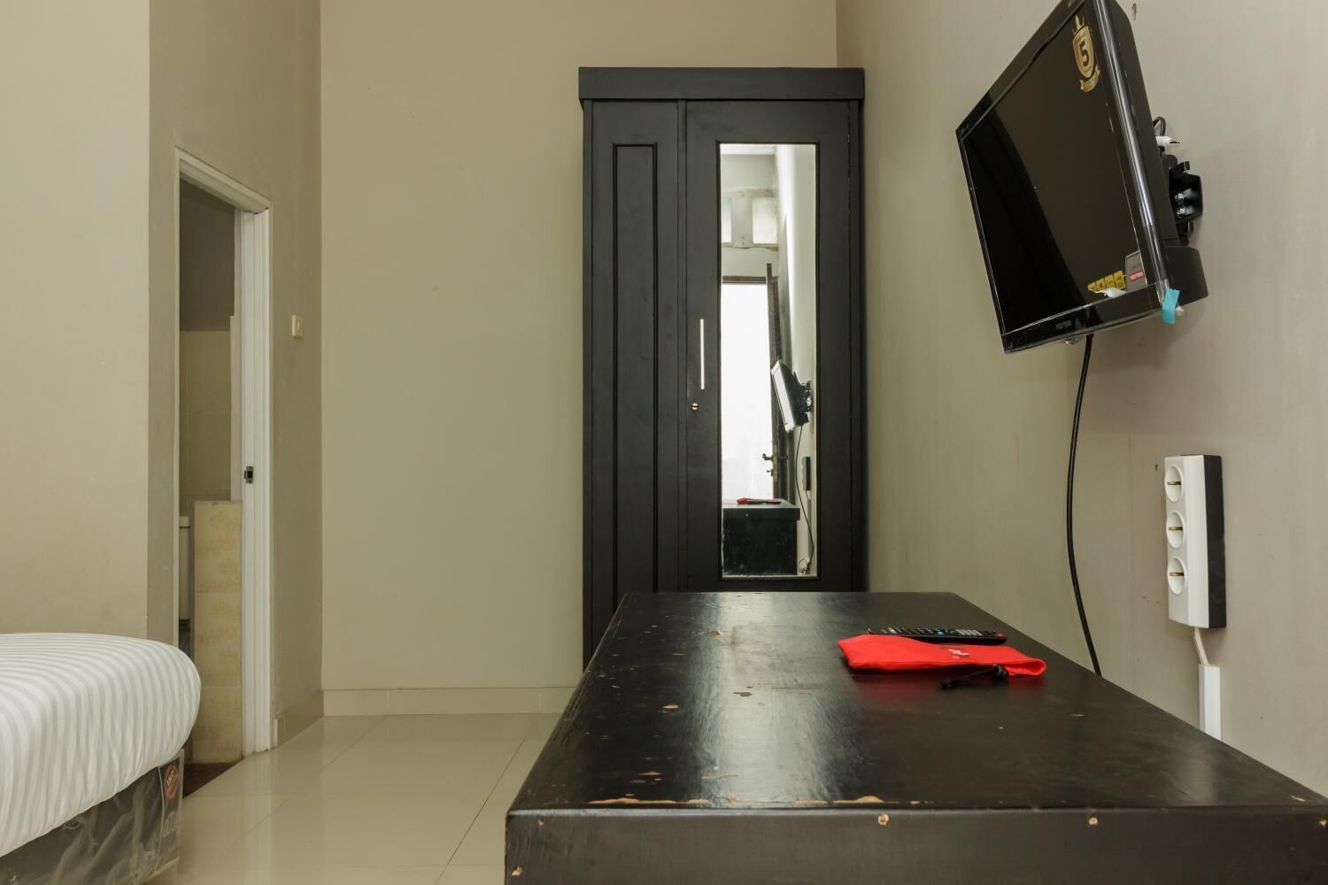 A hotel room with a bed, a desk, a television mounted on the wall, and a door leading to another room.