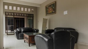 A room with a black leather sofa, a wooden coffee table, and a glass door leading outside. - RedDoorz Syariah near Taman Air Mancur Bogor (Bogor)