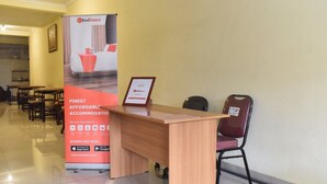 Un comptoir d’accueil orné d’une enseigne RedDoorz, d’un certificat encadré et d’une chaise rouge.