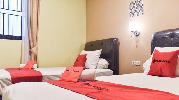 Une chambre d’hôtel avec deux lits, chacun étant équipé d’une couverture et de coussins rouges, ainsi que d’une tête de lit.