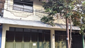 Un immeuble doté d’une entrée fermée par un portail, d’un balcon et d’un arbre devant.