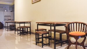 Un coin repas avec des tables et des chaises en bois, une cuisine à l’arrière-plan et un tableau encadré au mur.