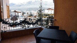 A balcony with a table and chairs, overlooking a snowy mountain and a town with buildings and a sign that reads "CAFFÈ CRISTAL." - Hotel Cristallo (Andalo)