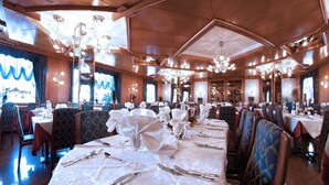 A restaurant with multiple tables set for dining, featuring chandeliers and wooden paneling. - Hotel Cristallo (Andalo)