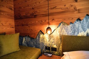 A cozy room with wooden walls, a bed with a green headboard, and a wall mural of a mountain. - Hotel Cristallo (Andalo)