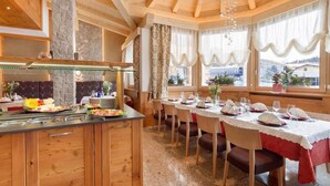 A restaurant with a long dining table, wooden chairs, and a buffet area with various dishes. - Hotel Cristallo (Andalo)