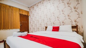 A hotel room with a neatly made bed, a red and white bedspread, a wooden headboard, and a patterned wallpaper. - RedDoorz Plus @ Jalan Parangtritis 2 (Sewon)