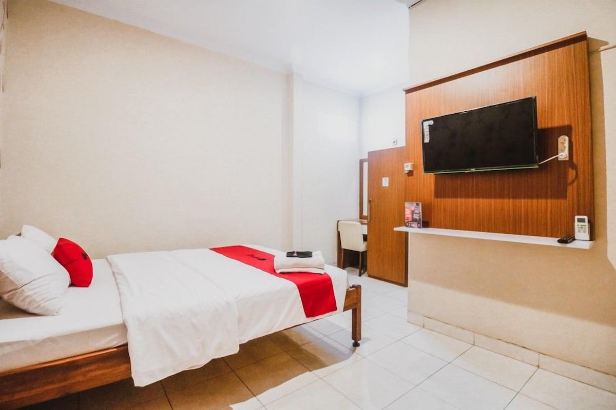 Una habitación de hotel con una cama, un televisor montado en la pared, un escritorio y una silla.