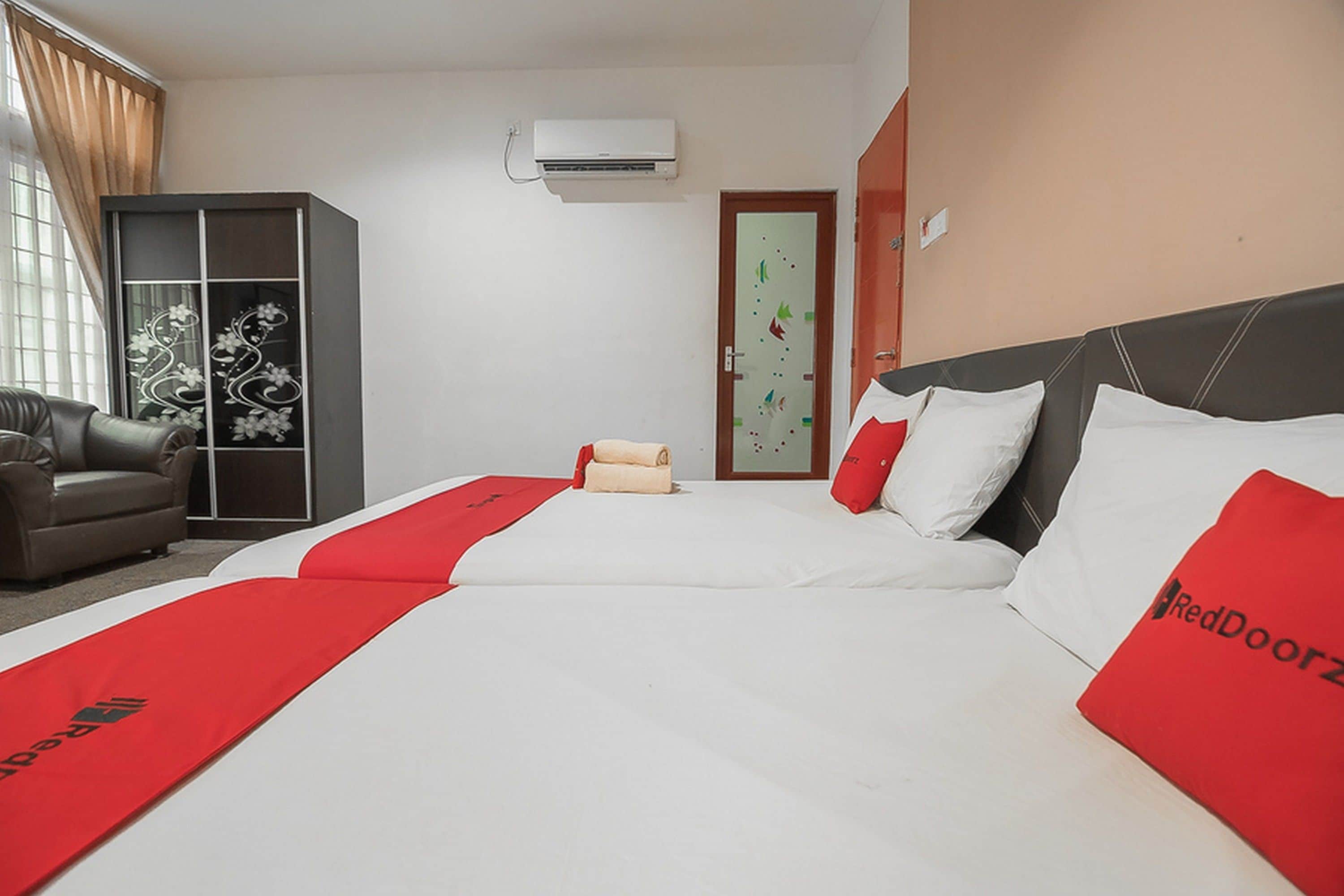 A hotel room with a large bed, a sofa, a wardrobe, and an air conditioning unit.
