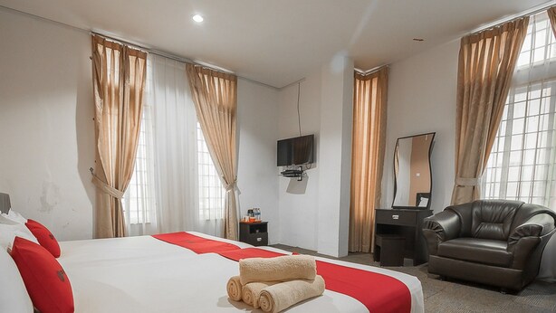 Une chambre d’hôtel avec un grand lit, un bureau, un fauteuil en cuir, une télévision et des rideaux.