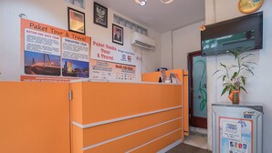 Un comptoir d’accueil avec des panneaux orange, une horloge et une plante. On y trouve des affiches faisant la publicité de circuits touristiques et de forfaits de voyage.