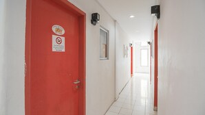 Un couloir aux portes rouges, aux murs blancs et au sol carrelé.