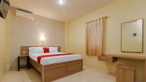 A hotel room with a wooden bed, a bedside table, a desk with a mirror, and an air conditioning unit.