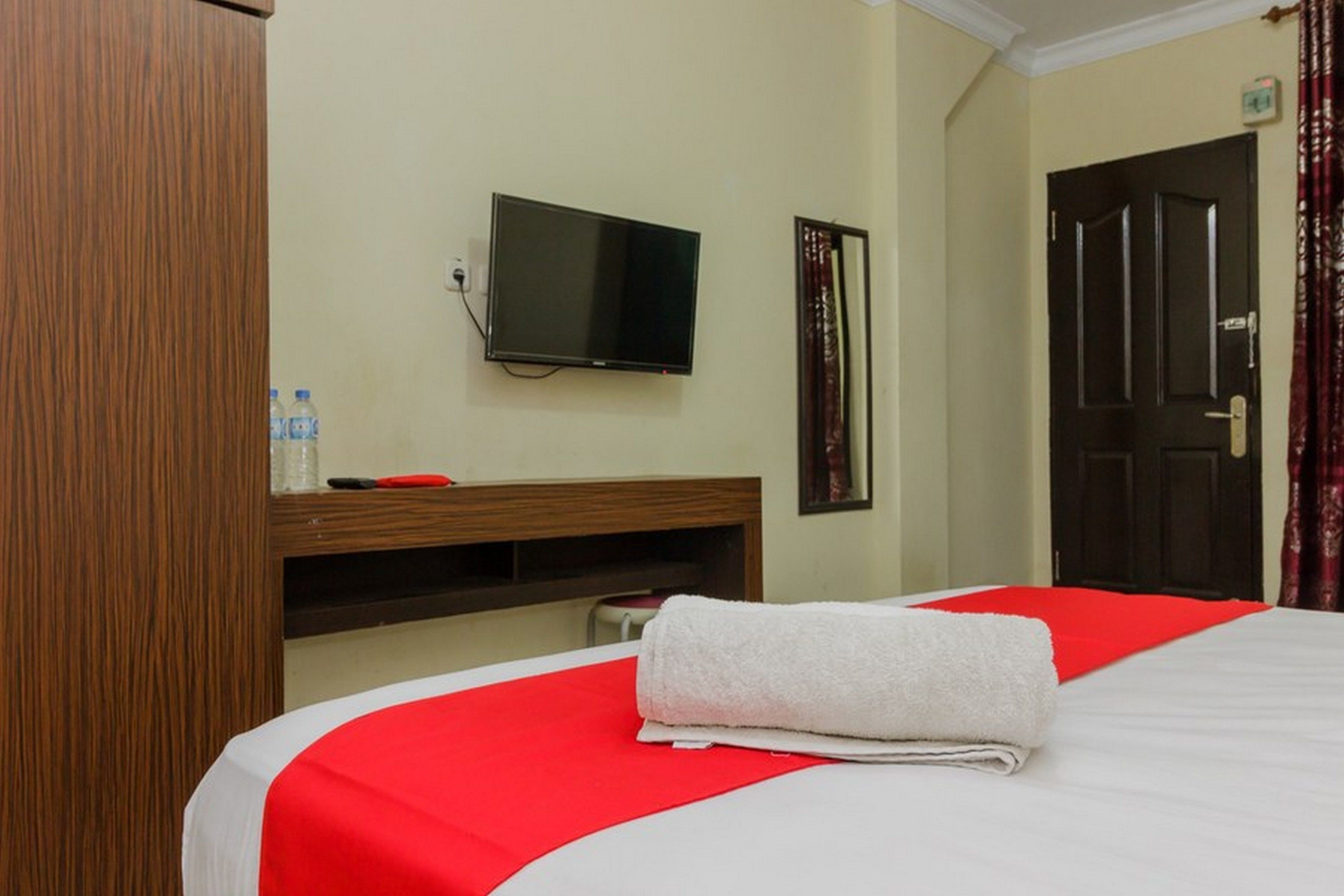 Une chambre d’hôtel avec un lit, un téléviseur fixé au mur, une armoire et une porte.