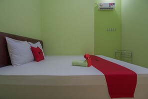 A single-bed room with a red and white pillow, a red towel, and a red bed runner. An air conditioning unit is mounted on the wall above the bed. - RedDoorz near Kampus UMP Purwokerto (Purwokerto)