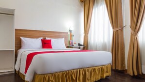 A neatly made bed with white and red bedding, a wooden headboard, and a bedside table with a lamp. - RedDoorz Plus @ Surapati 2 (Bandung)
