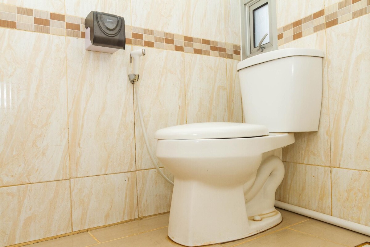 A bathroom with a toilet, a hand dryer, and a tiled wall.