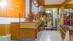 A reception area with a wooden reception desk, a staircase, and a display of colorful textiles. - RedDoorz Plus @ Surapati 2 (Bandung)