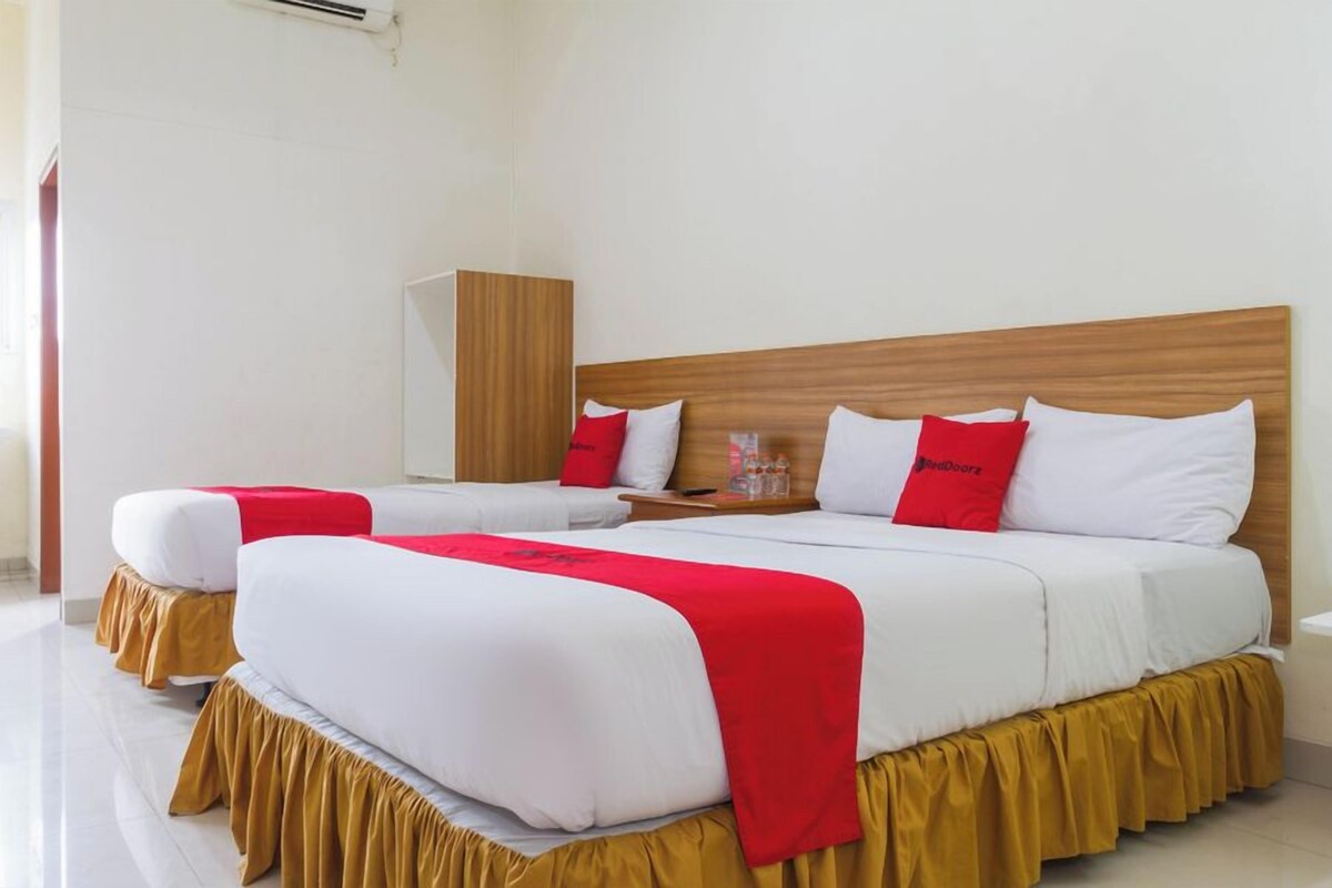 A hotel room with two beds, each with white bedding and red accents, a wooden headboard, and a small bedside table with a glass.