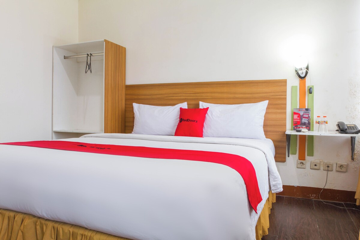 Una habitación de hotel con cama, mesita de noche, espejo y lámpara de pared.