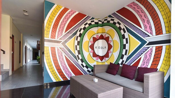 A lobby with a colorful wall mural, a wicker sofa with cushions, and a small table. - RedDoorz near Legian Street (Legian)