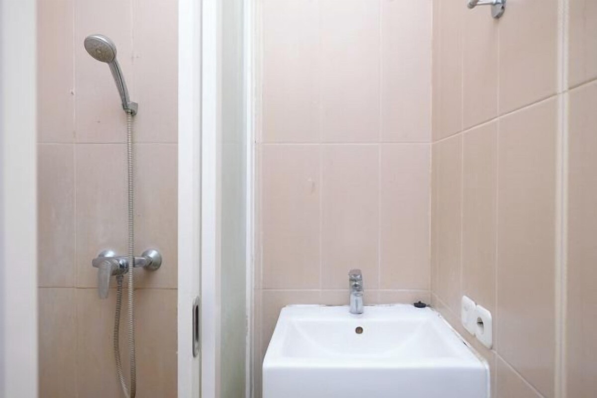 A bathroom with a shower, a sink, and beige tiled walls.