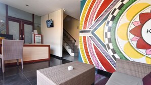 A hotel reception area with a reception desk, wicker furniture, a staircase, and a colorful wall mural. - RedDoorz near Legian Street (Legian)
