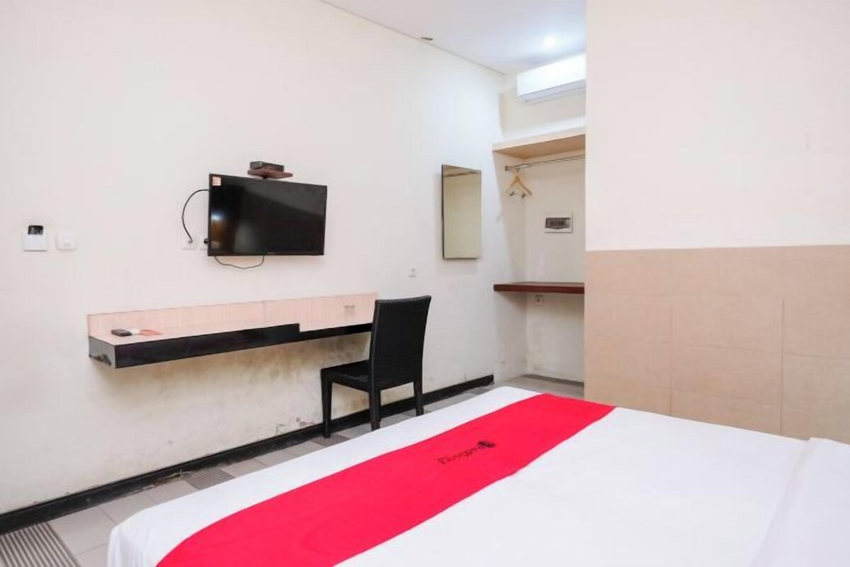 Quarto de hotel com cama, escrivaninha, cadeira, TV fixada na parede e espelho sobre outro espelho.