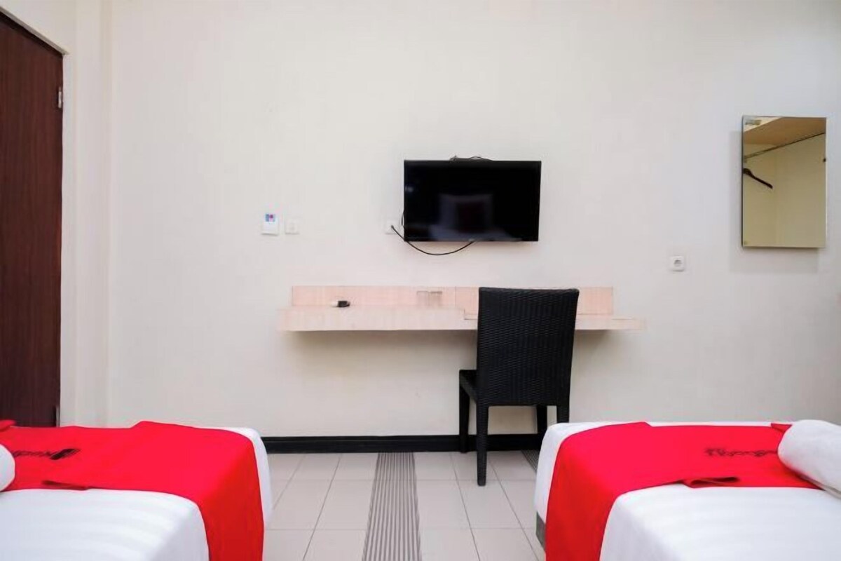 A hotel room with two beds, a desk, a chair, a television, and a mirror.