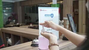 A person using a hand sanitizer dispenser at a hotel reception desk with a sign indicating RedDoorz and HygienePass certification. - RedDoorz near Jogja City Mall 3 (Pogung Lor)