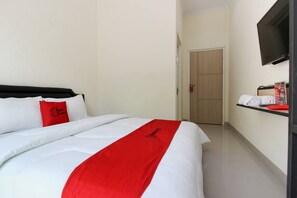 A hotel room with a bed, a red pillow, a television mounted on the wall, and a door in the background. - RedDoorz near Jogja City Mall 3 (Pogung Lor)