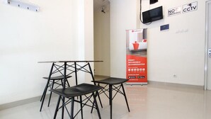 A hotel room with a modern design, featuring a minimalist table and chairs arrangement, a flat-screen TV mounted on the wall, and a red promotional stand. - RedDoorz near Jogja City Mall 3 (Pogung Lor)