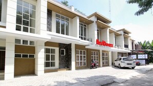 A modern building with a prominent 'RedDoorz' sign, featuring a clean, white facade with large windows and a stone accent wall. - RedDoorz near Jogja City Mall 3 (Pogung Lor)
