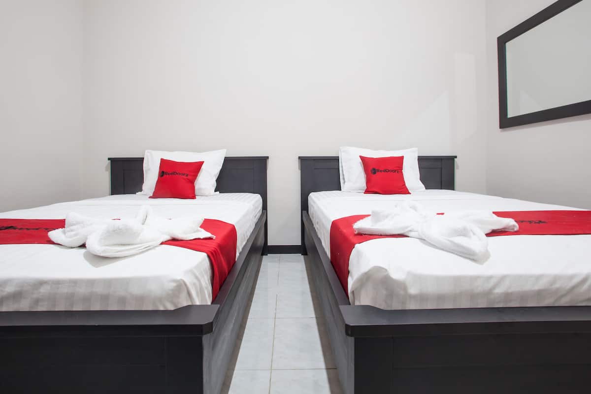 Dos camas individuales con ropa blanca y detalles rojos, un cabecero oscuro y una toalla roja sobre cada cama.