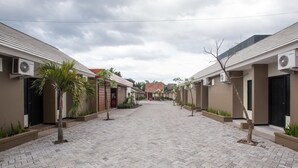 A courtyard with a paved walkway, lined with buildings featuring air conditioning units and small trees. - RedDoorz Plus near Banyuwangi Airport (Rogojampi)
