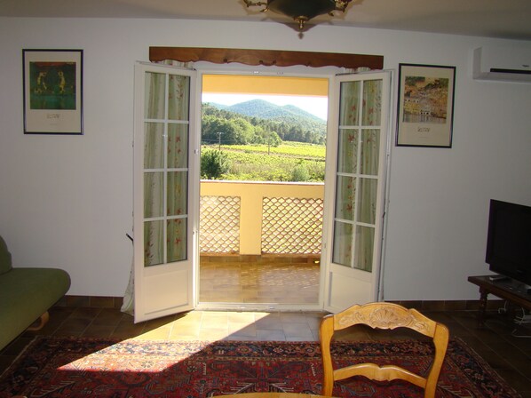 Puerta abierta que da a un balcón con vistas a un paisaje verde.