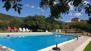 A swimming pool with lounge chairs, a stone sculpture, and a view of a hill and building in the background.
