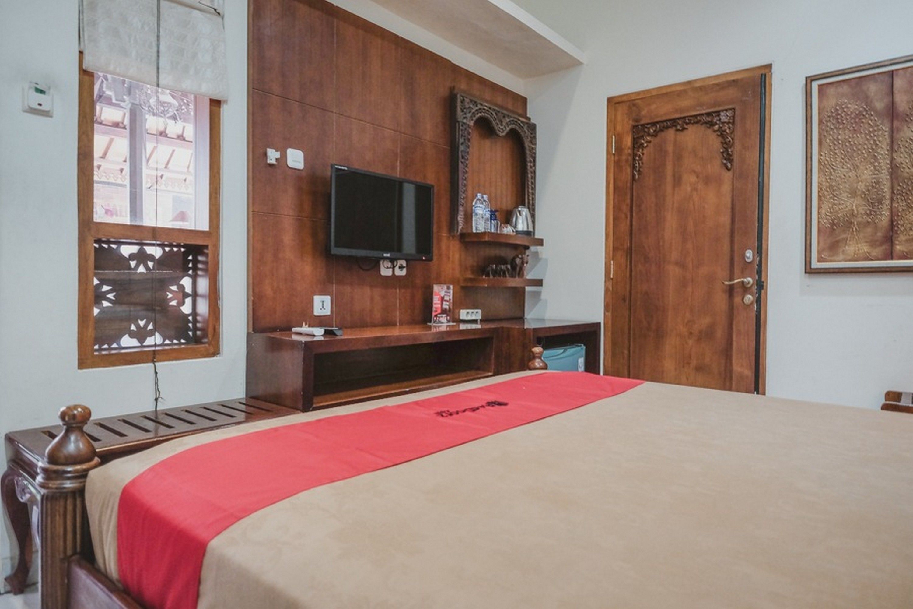Un dormitorio con cama, armario de madera, televisor y una puerta con panel decorativo.