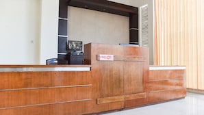 A reception desk with a wooden finish, a sign indicating 'Free Wi-Fi', and a television on a shelf above. - RedDoorz near Alun Alun Wonosobo (Wonosobo)