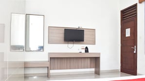 A hotel room with a bed, a TV mounted on the wall, a wooden desk, and a door. - RedDoorz near Alun Alun Wonosobo (Wonosobo)